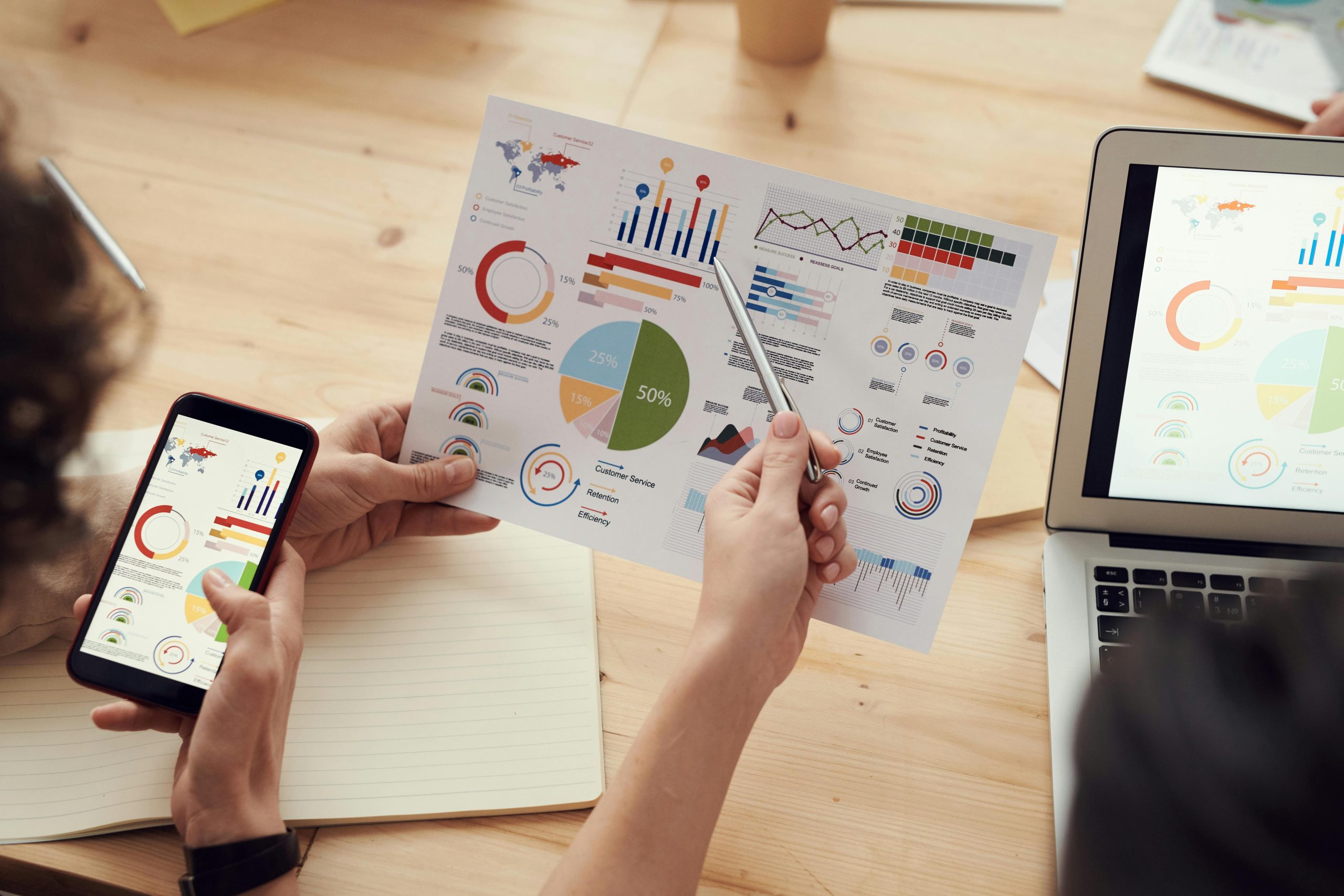 Two people reviewing colorful charts on a printout and phone at a desk, aligning on a plan they can actually use