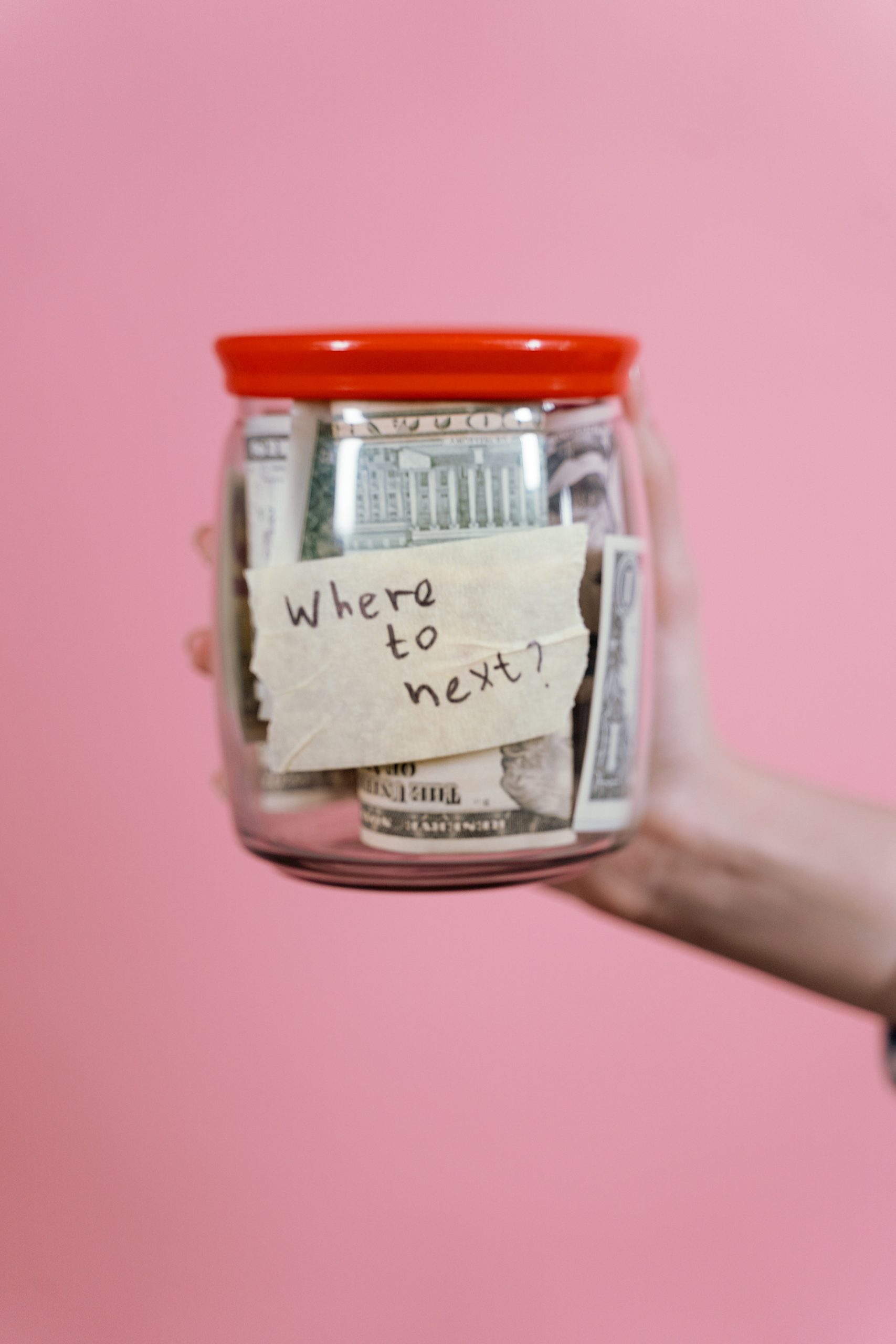 Hand holding a donation jar with a "Where to next?" note, reflecting fundraising support with heart and structure