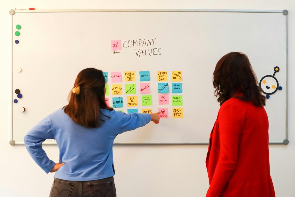 Two colleagues reviewing a "Company Values" board of sticky notes, the kind of meaningful work that deserves to be seen, felt, and chosen